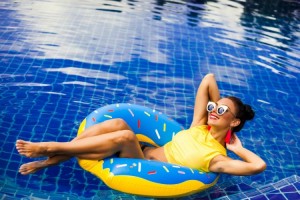 femeie pe un colac in forma de gogoasa intr-o piscina